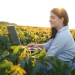 Female farmer or agronomist examining green soybean plants in field.